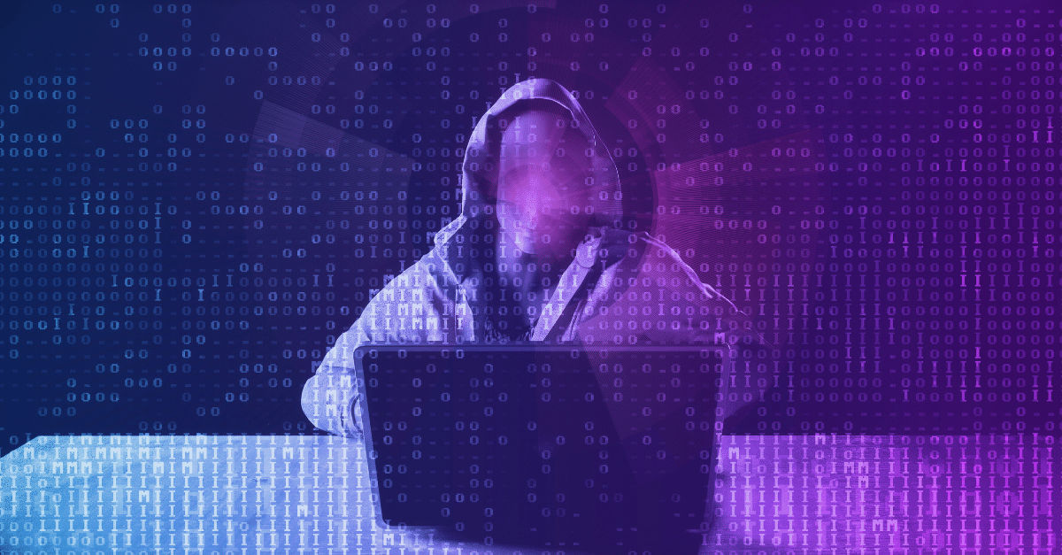 a person in a hoodie sitting at a table with a laptop