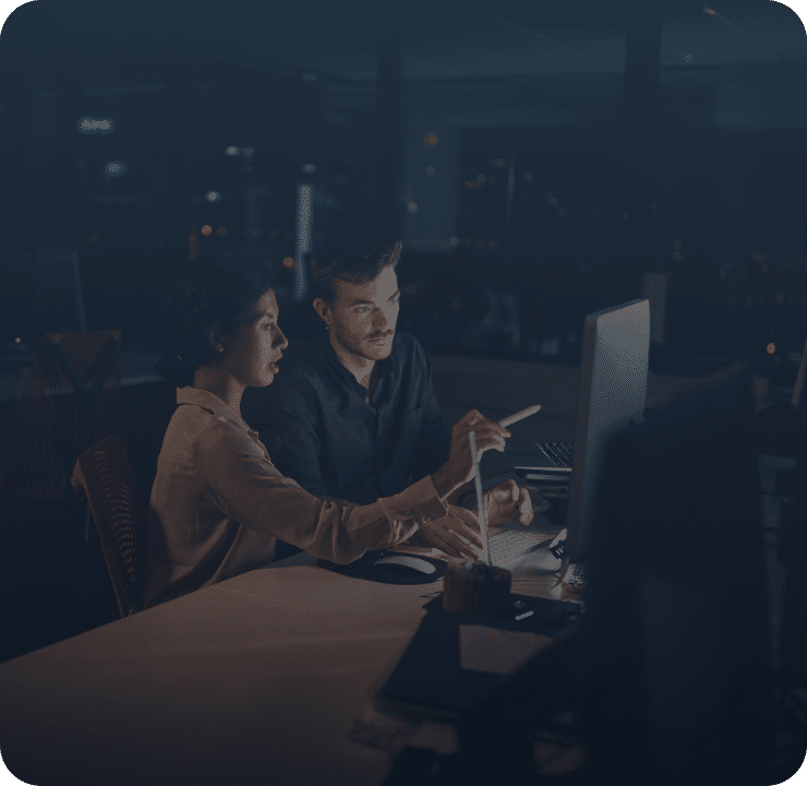 Woman pointing man to computer screen in dark office